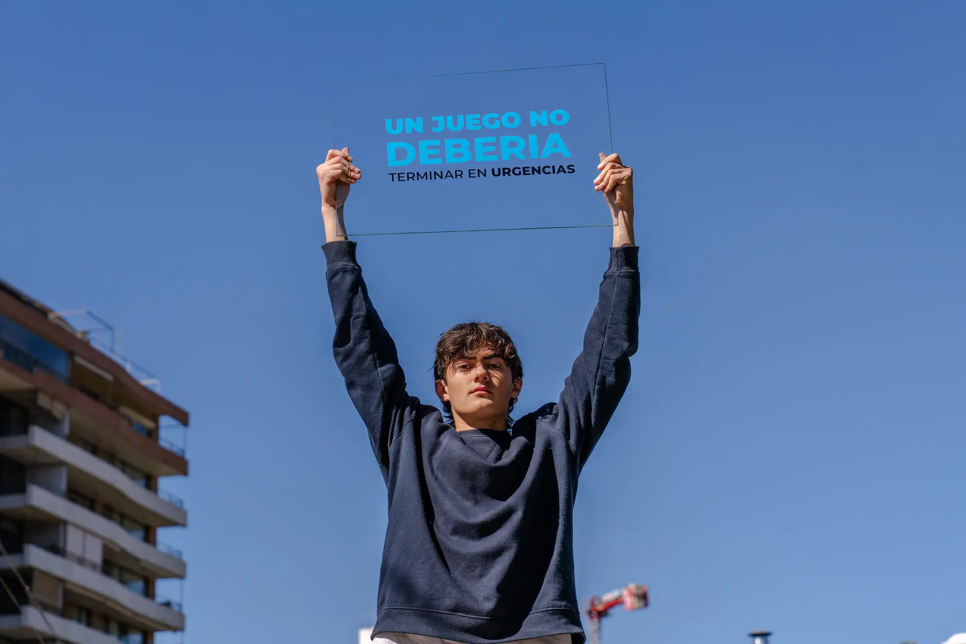 Joven levantando un panel de vidrio con la frase: Un juego no debería terminar en urgencias